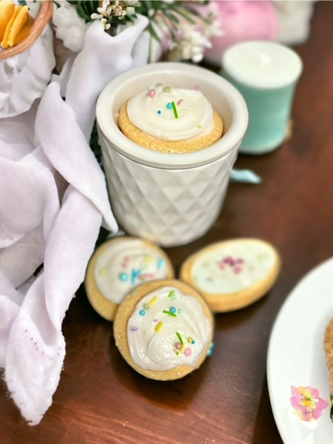 wax melts that look like sugar cookies with white frosting and spring colored sprinkles on a wooden counter and 1 in a wax warmer that is white