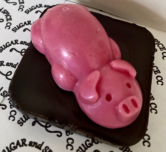 a wax shaped pink pig on a brown wax square with a background that says sugar and spice cc
